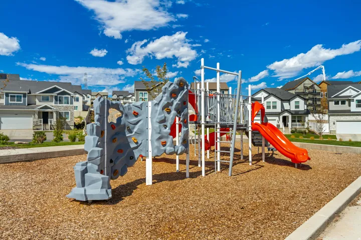 Community playground with a rock climbing wall, slide, and wood chip ground cover