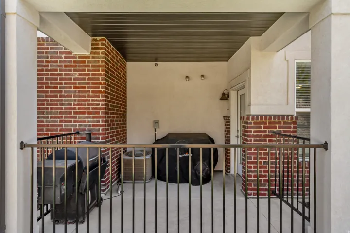 Covered outdoor patio with a bronze-finish railing, brick siding, and stucco walls