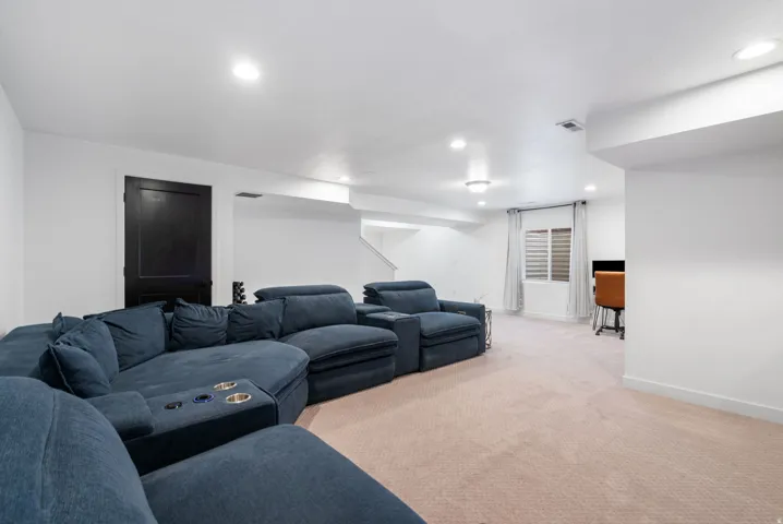 Recessed lighting throughout, light-colored carpeting, white wall finishes, and a dark-paneled door
