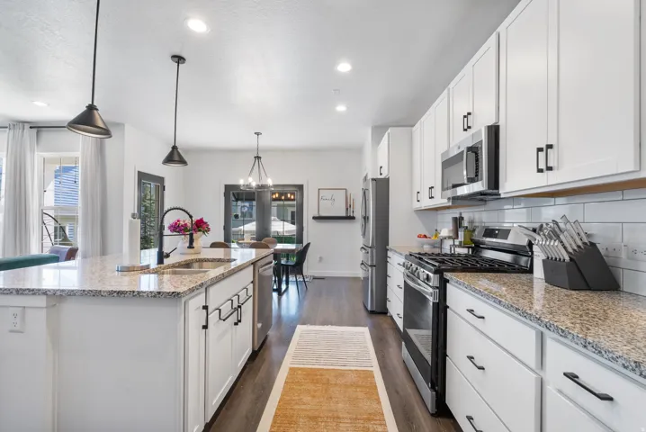 Kitchen featuring white cabinetry, stainless steel appliances, speckled countertops, a subway tile backsplash, and an island with an undermount sink