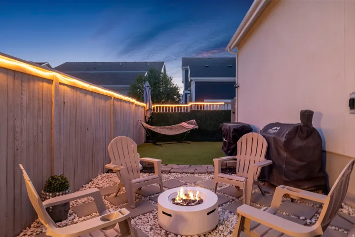 Enclosed backyard featuring a fire pit, artificial turf, and privacy fencing with integrated lighting