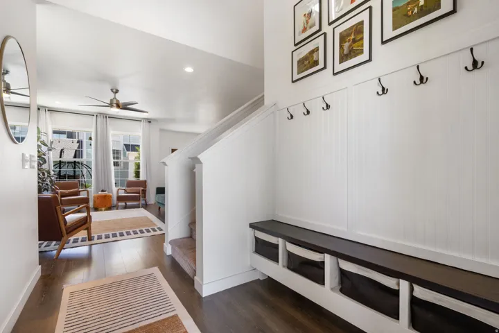 Entry area featuring a built-in bench with integrated storage, vertical paneling with coat hooks, wood-finish flooring, and a ceiling fan in the adjacent space
