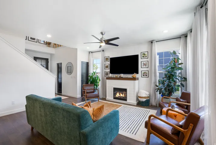 Living area with wood-finish flooring, a contemporary fireplace with a wooden mantel, and a ceiling fan