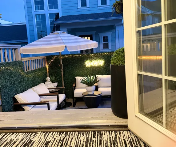 Outdoor patio space featuring a striped umbrella, privacy screening, and wood-framed seating