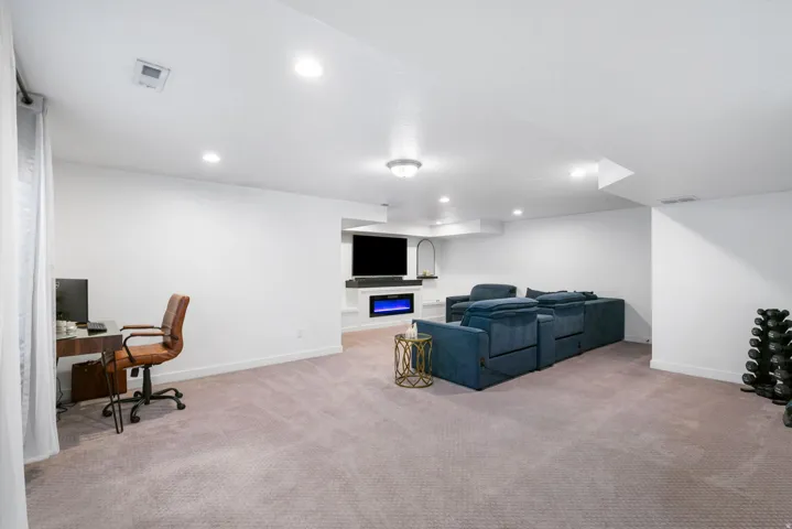 Recessed ceiling lights, integrated fireplace feature, built-in shelving, carpeted flooring, and a window with sheer curtains