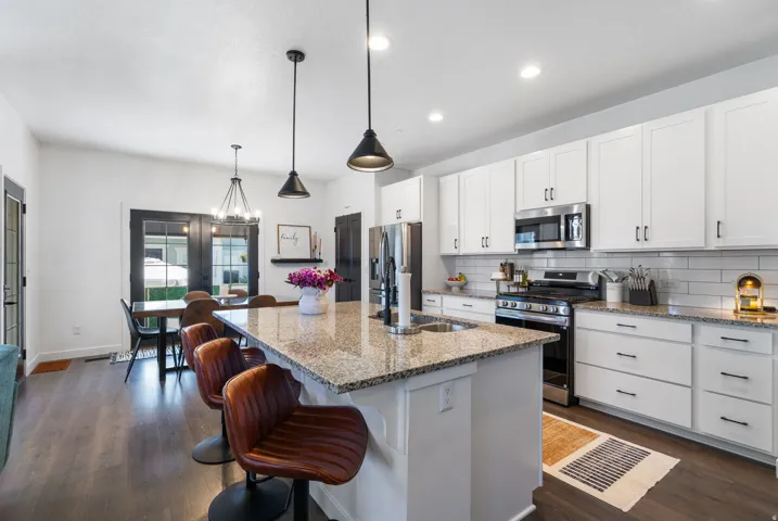 Kitchen featuring a large island with sink, white shaker cabinetry, stainless steel appliances, and wood-finish flooring