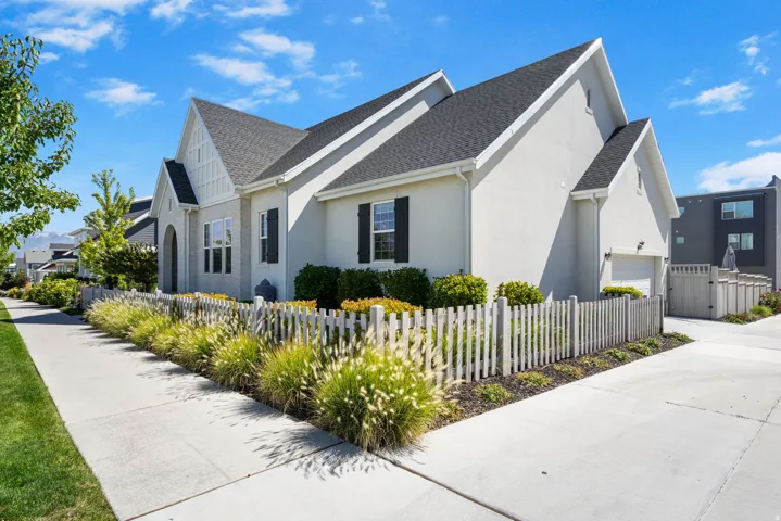 Contemporary stucco exterior with a dark shingle roof, white trim, and a white picket fence