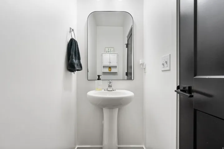 Pedestal sink with chrome faucet, framed mirror, and a wall-mounted cabinet