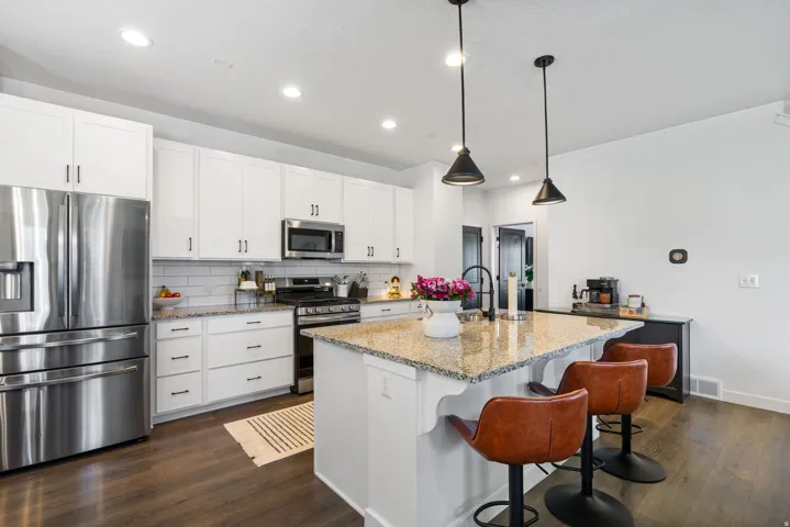 Kitchen featuring a large island with granite countertop, white cabinetry with black hardware, stainless steel appliances, and dark wood-finish flooring