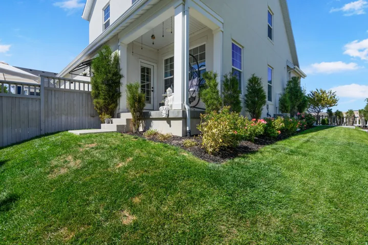 Stucco exterior featuring multiple windows, a covered porch, a privacy fence, and manicured landscaping with green grass