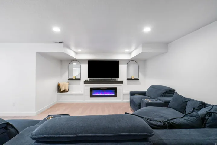 Recessed lighting illuminating the white walls, built-in entertainment center, electric fireplace, arched wall niches, and light-colored carpet