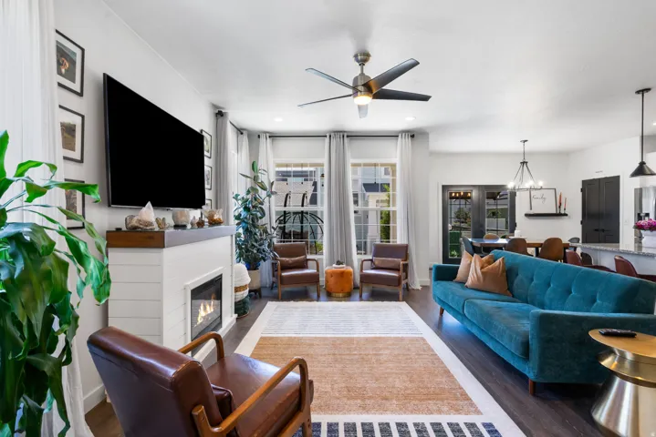 Living area featuring wood-finish flooring, a contemporary ceiling fan, and a shiplap fireplace with a wood mantel