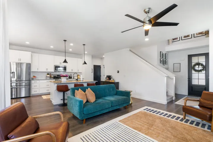 Open-concept living area featuring wood-finish flooring, a contemporary ceiling fan, and a kitchen with white cabinetry, stainless steel appliances, and a central island