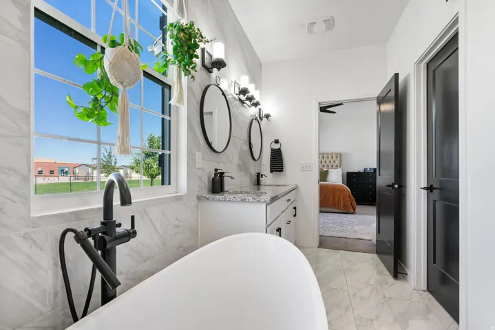 Freestanding tub with floor-mounted faucet, dual vanity with granite countertops, black framed mirrors, and tile flooring