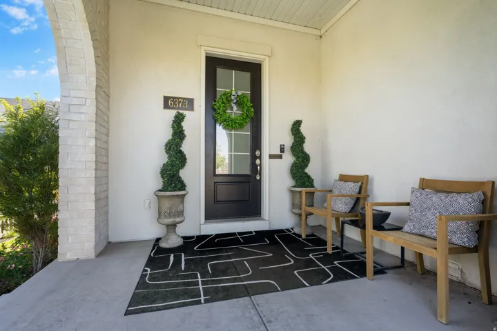 Covered concrete porch with a stone archway, stucco exterior, and a dark paneled entry door with glass inserts