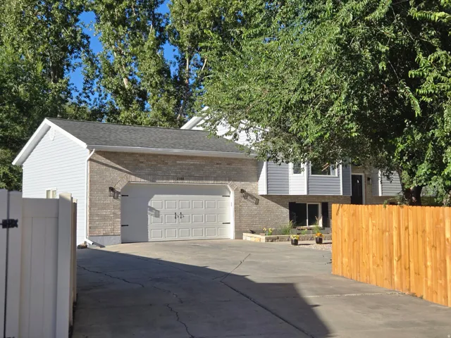 Two-car garage with carriage-style doors, brick and siding exterior, asphalt driveway, wood privacy fence, and white vinyl fencing