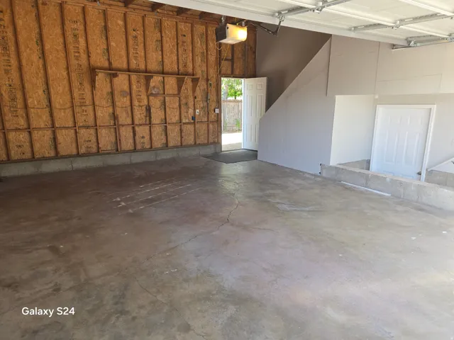 Spacious garage with exposed wood-panel walls, concrete flooring, and a white overhead garage door