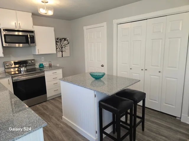 Kitchen featuring white cabinetry, granite countertops, stainless steel appliances, a center island with beadboard paneling, and wood-finish flooring