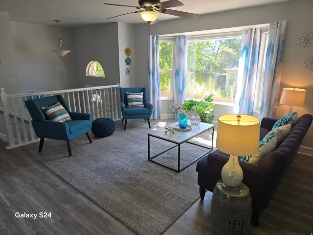 Wood-finish flooring, bay window, ceiling fan, white spindle railing, and arched window feature