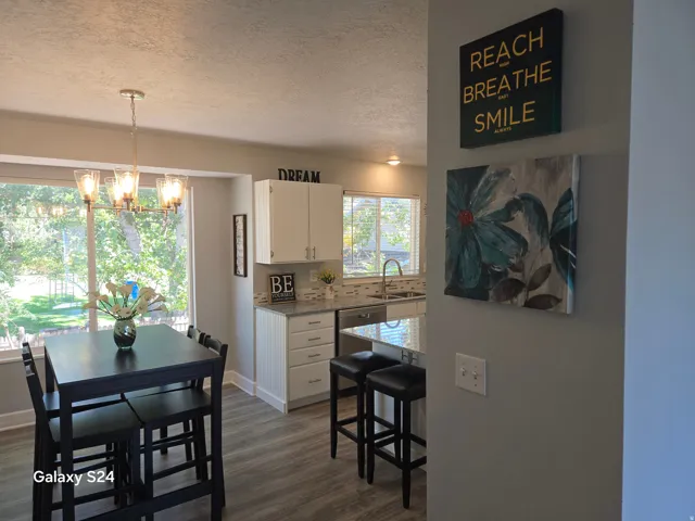 Wood-finish flooring throughout, bright kitchen with white cabinetry, stainless steel sink with gooseneck faucet, light-toned countertop, and tile backsplash