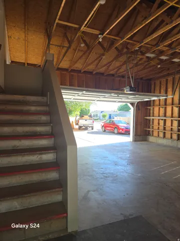 Exposed wood-framed ceiling with visible rafters, concrete flooring, and a partially open garage door
