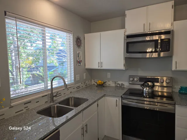 White cabinetry, stainless steel appliances, dual basin sink, stone countertops, and a full tile backsplash