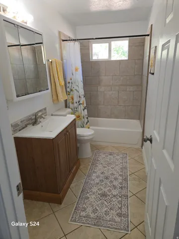 Bathroom featuring a wood-finish vanity with an integrated sink, tiled flooring, and a tiled shower surround