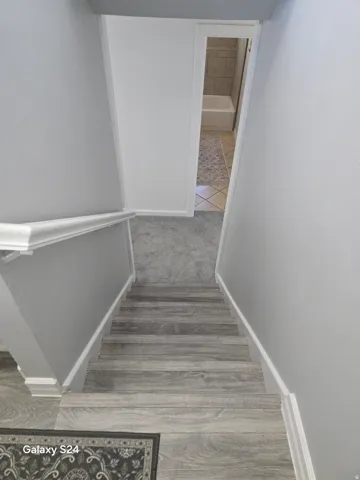 Wood-finish stair treads with white risers and handrail, gray wall color