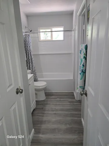 White bathtub with white tiled surround, window, and wood-finish flooring