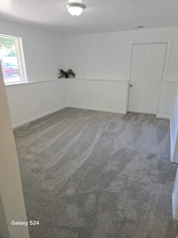 Spacious room featuring light gray carpeting, white walls, and a white paneled door