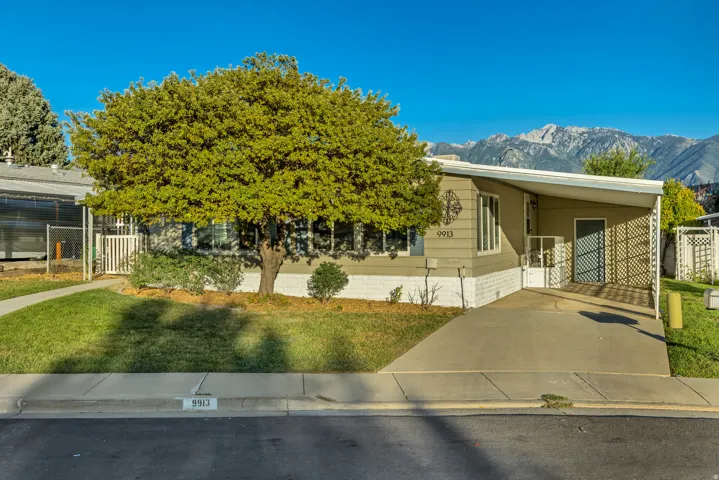 Single-story property with a covered carport, mature front tree, and mountain backdrop