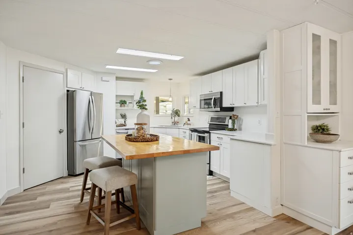Kitchen featuring white cabinetry, wood-finish flooring, stainless steel appliances, a center island with a wood countertop, and ample counter space