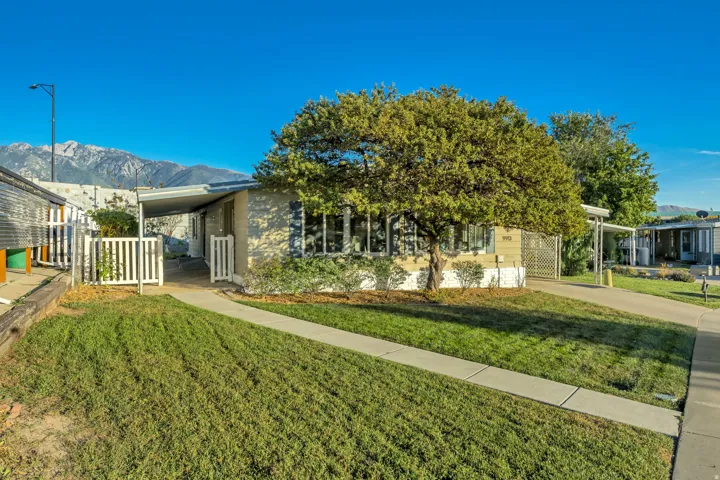 Property exterior featuring a mature tree, paved walkway, and a covered carport