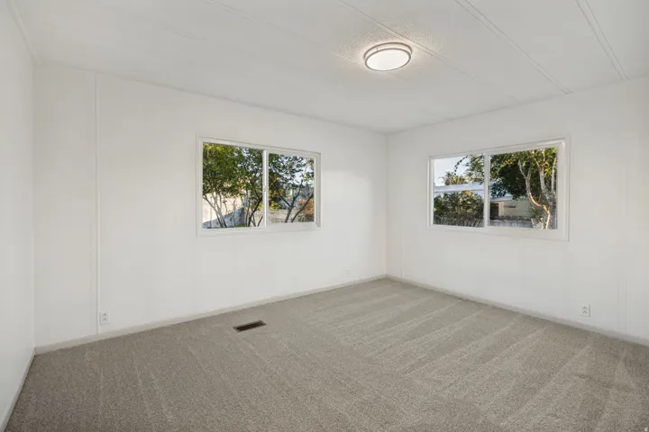 Large Bedroom featuring light gray carpeting, white walls, two windows, and a flush-mount ceiling light fixture