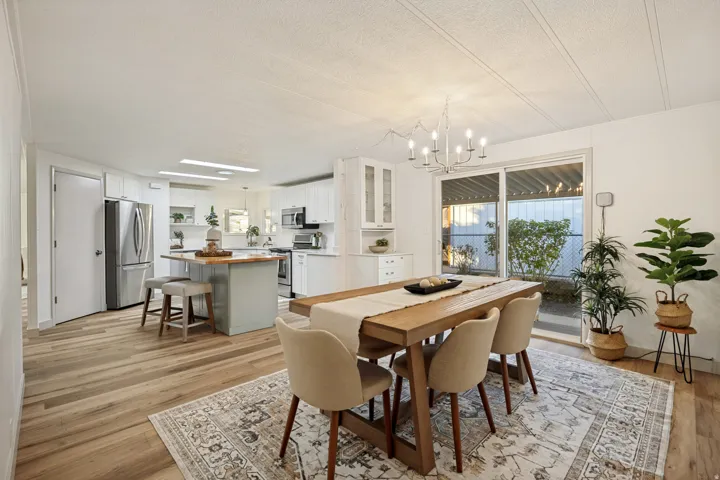 Wood-finish flooring throughout, kitchen with white cabinetry and stainless steel appliances, central island with wood countertop, dining area with modern chandelier, and sliding glass door