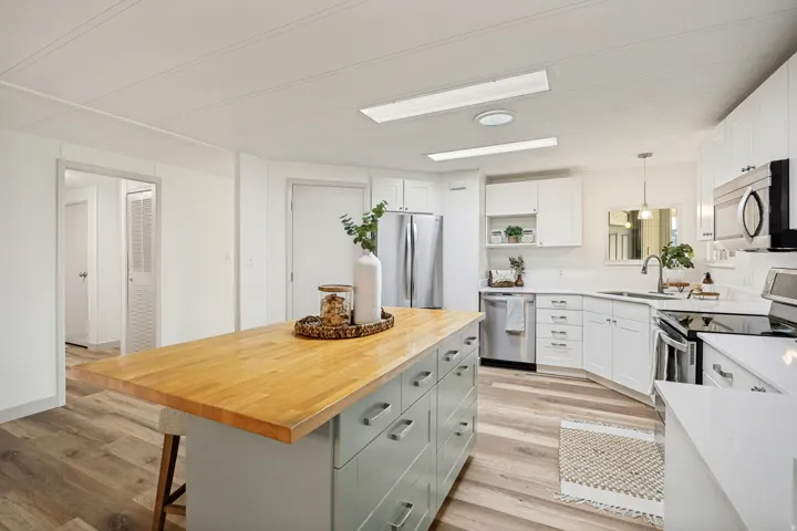 Kitchen featuring white cabinetry, stainless steel appliances, wood-finish flooring, a light-colored countertop, and a center island with a butcher block surface
