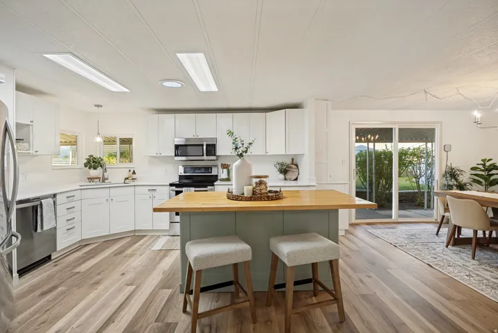 Modern kitchen featuring white cabinetry, stainless steel appliances, wood-finish flooring, a center island with a wood countertop, and sliding glass doors