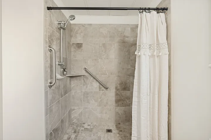 Primary Bathroom with Tiled shower featuring a handheld showerhead, built-in shelving, and grab bars. Curbless for wheel chair accessibility.
