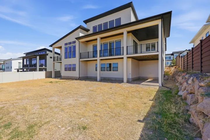 Contemporary architectural style with multiple levels, extensive fenestration, black exterior trim, upper-level balconies with black railings, and a lower-level covered patio area