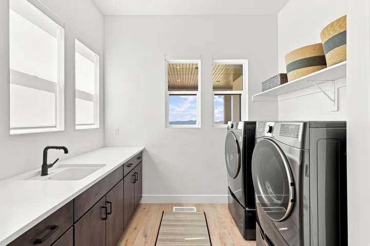Bright utility room featuring wood-finish flooring, a white countertop with an integrated sink, dark wood-finish cabinetry, and multiple windows
