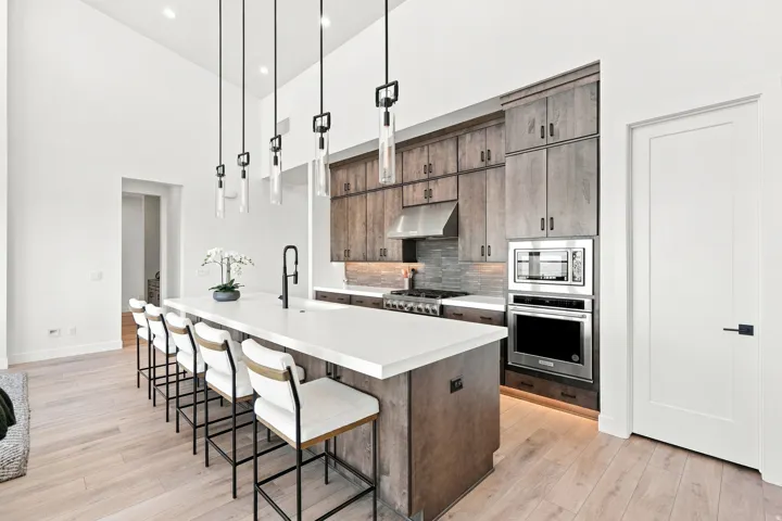 Spacious kitchen with a large central island, stainless steel appliances, wood-finish cabinetry, a tile backsplash, and wood-finish flooring