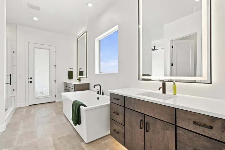 Freestanding soaking tub, dual floating vanities with integrated sinks, back-lit mirrors, and walk-in shower with glass enclosure