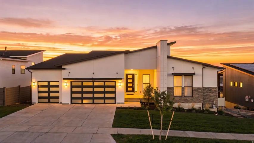 Contemporary architectural style featuring a split-level roofline, stone facade accents, two-car garage with frosted glass panels, concrete driveway, and front entryway with a paneled door