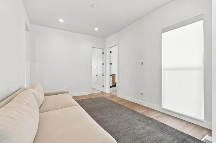 Recessed lighting, light wood-finish flooring, white walls, and a large window with roller shades