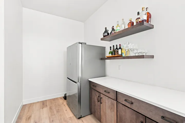 Built-in cabinetry with dark wood finish, white countertop, stainless steel refrigerator, and wood-finish floating shelves