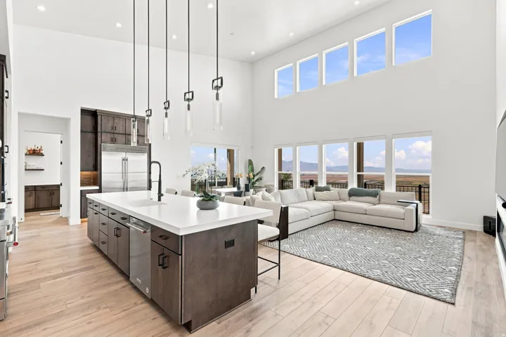 Open concept great room with high ceilings, large windows, a spacious kitchen island, and wood-finish flooring