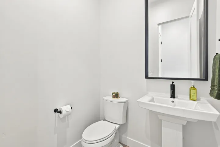 Pedestal sink with black matte faucet, rectangular framed mirror, and wood-finish flooring