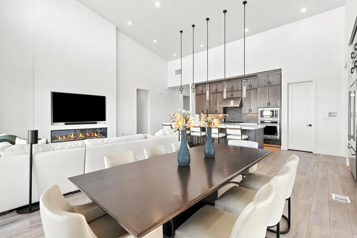 High ceilings with recessed lighting, linear fireplace with integrated television, wood-finish flooring, dark wood-tone cabinetry, and an island with bar seating