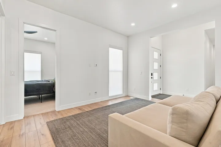 Wood-finish flooring throughout, modern entry door with frosted glass panels, recessed ceiling lighting, clean white walls, and a separate room access