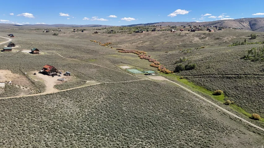Expansive property featuring a rustic-style residence, additional structures, a tennis court, and a meandering natural waterway